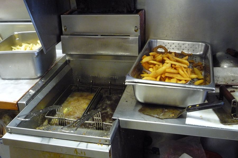 A working restaurant fryer with baskets in the oil and a pan of fries resting beside it