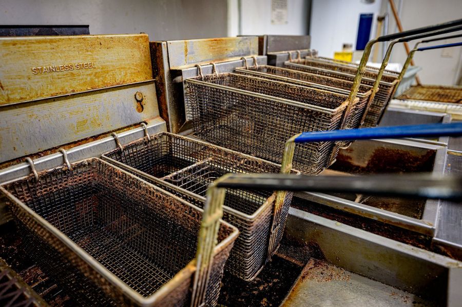 A row of commercial fryers with well-used, oil-stained baskets in a shared kitchen