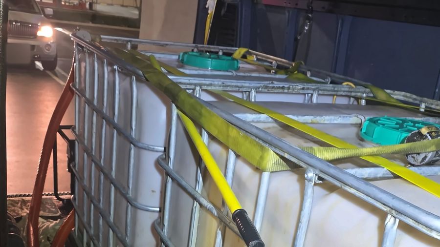 Two IBC totes of collected cooking oil strapped down with yellow ratchet straps inside a cargo van at night