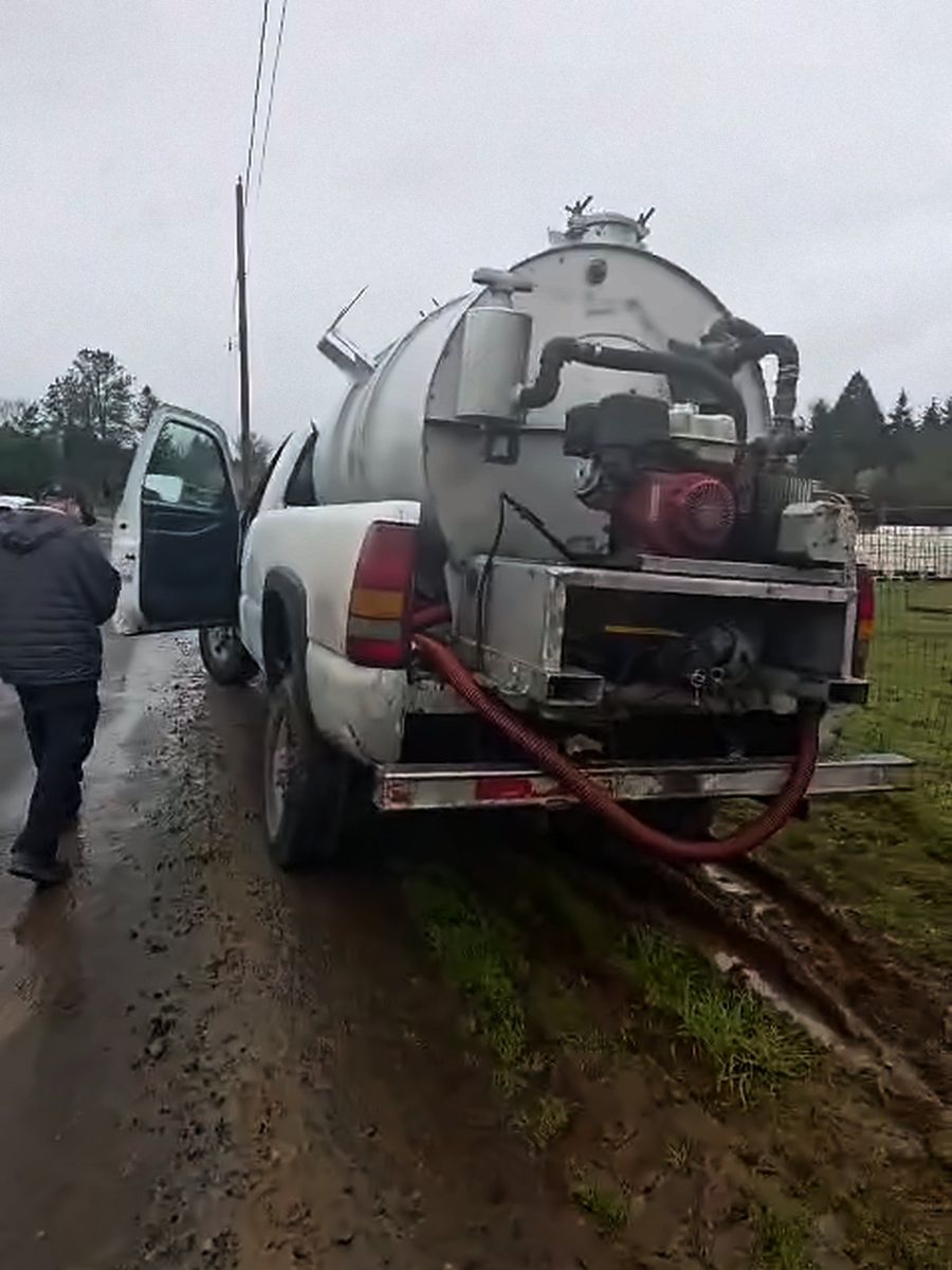 Pickup truck with a vacuum tank, pump and red suction hose on a muddy road
