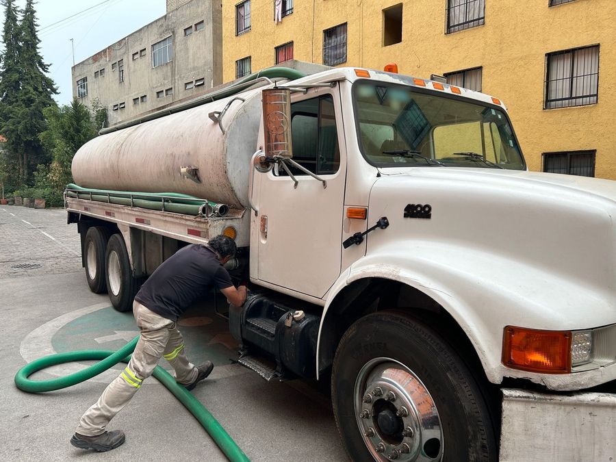 Worker connecting a green suction hose to a white tank truck